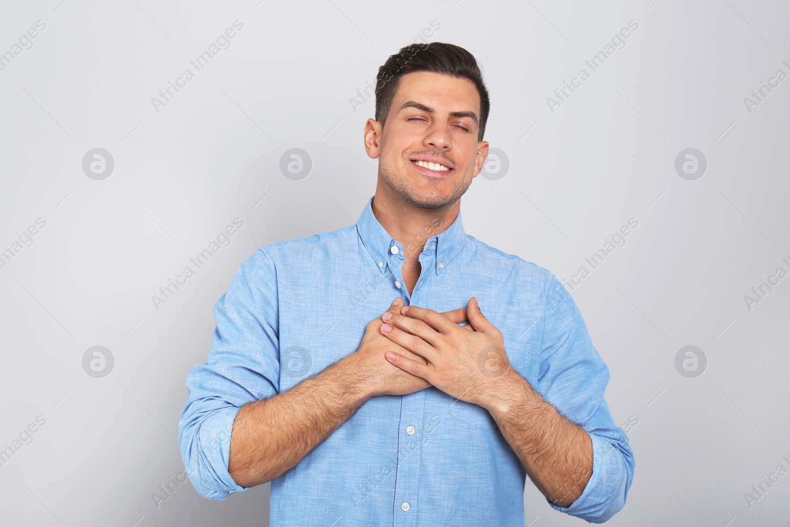 Photo of Handsome grateful man with hands on chest against light grey background