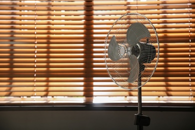 Modern electric fan near window indoors. Space for text