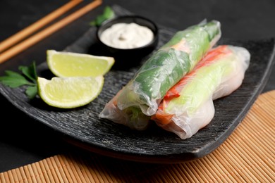 Photo of Delicious rolls wrapped in rice paper served on black table, closeup