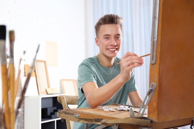 Photo of Teenage boy painting on easel in workshop, space for text. Hobby club