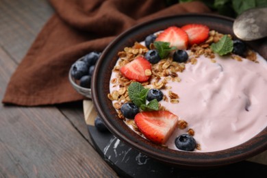 Photo of Bowl with yogurt, berries and granola on wooden table, closeup. Space for text