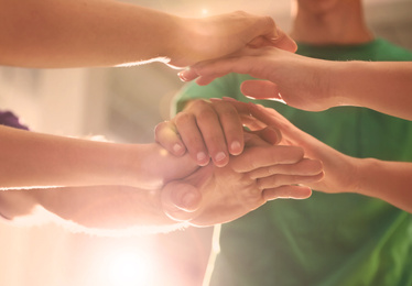 Image of Group of volunteers joining hands together in sunlit room, closeup