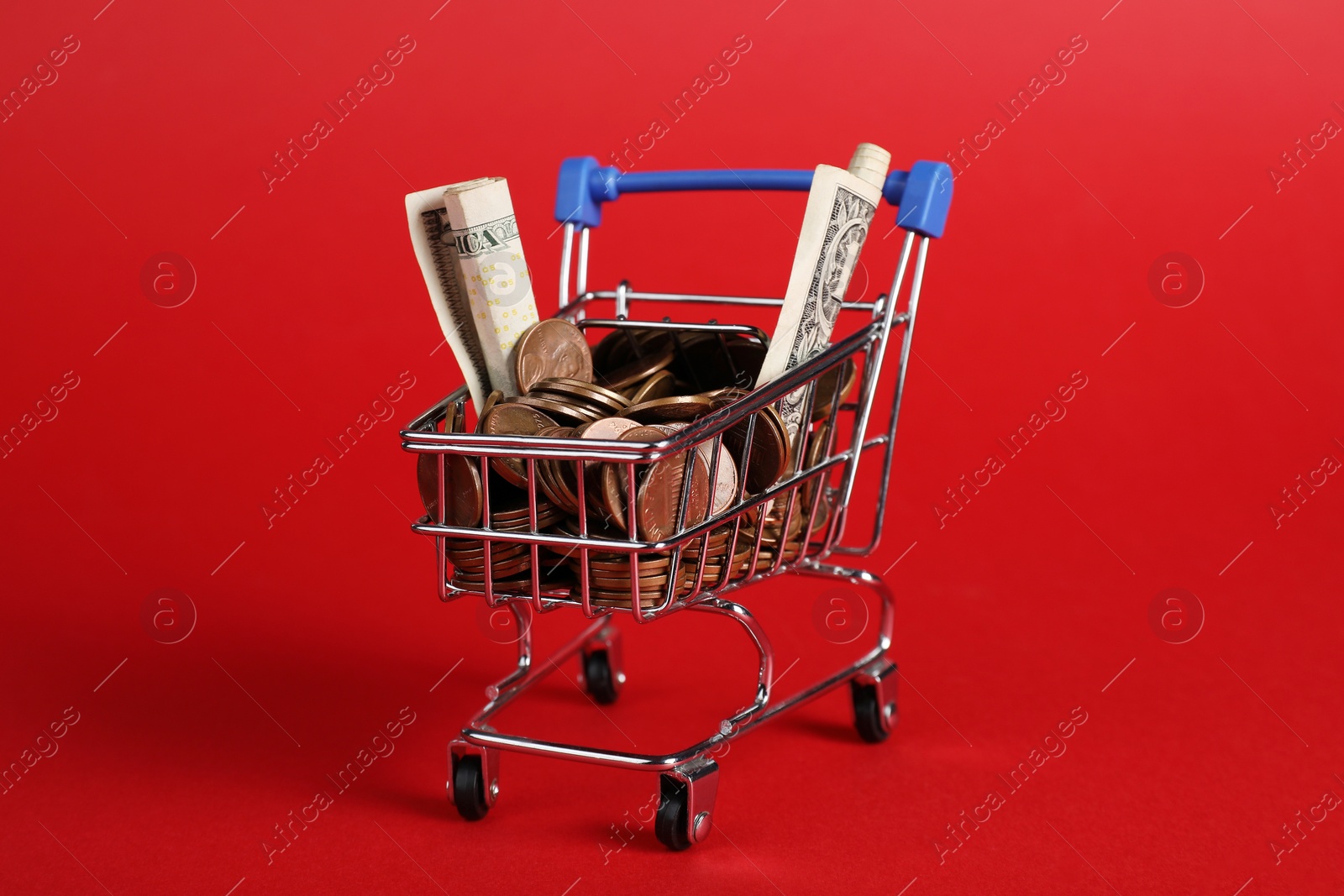 Photo of Small metal shopping cart with money on red background