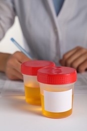 Photo of Closeup view of nurse writing urine analysis results at table, focus on container with sample