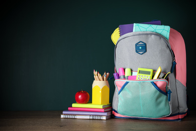 Stylish backpack with different school stationery on table against chalkboard. Space for text