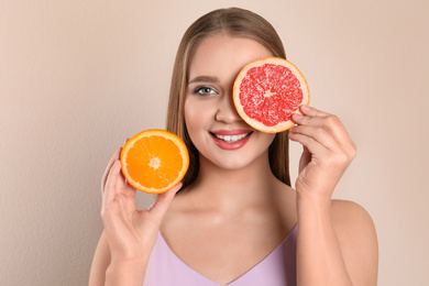 Photo of Young woman with cut orange and grapefruit on beige background. Vitamin rich food