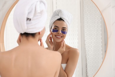 Photo of Beautiful young woman with under eye patches near mirror at home