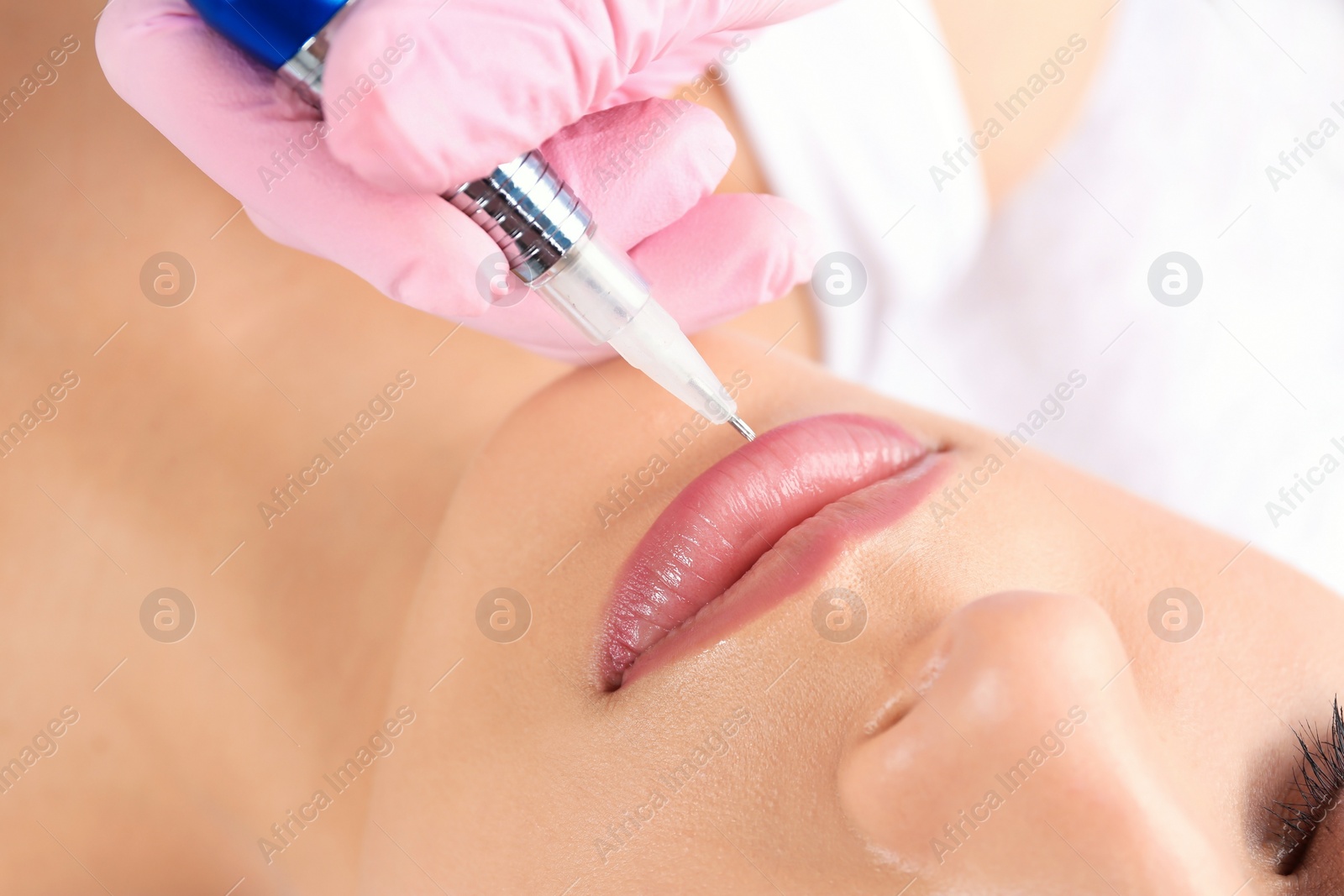 Photo of Young woman getting permanent makeup on lips in beautician salon, closeup