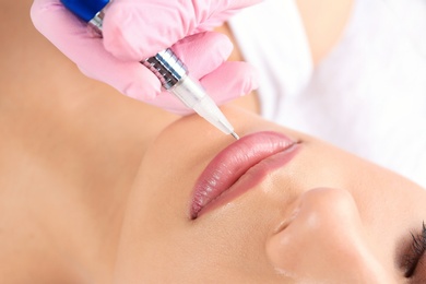 Photo of Young woman getting permanent makeup on lips in beautician salon, closeup
