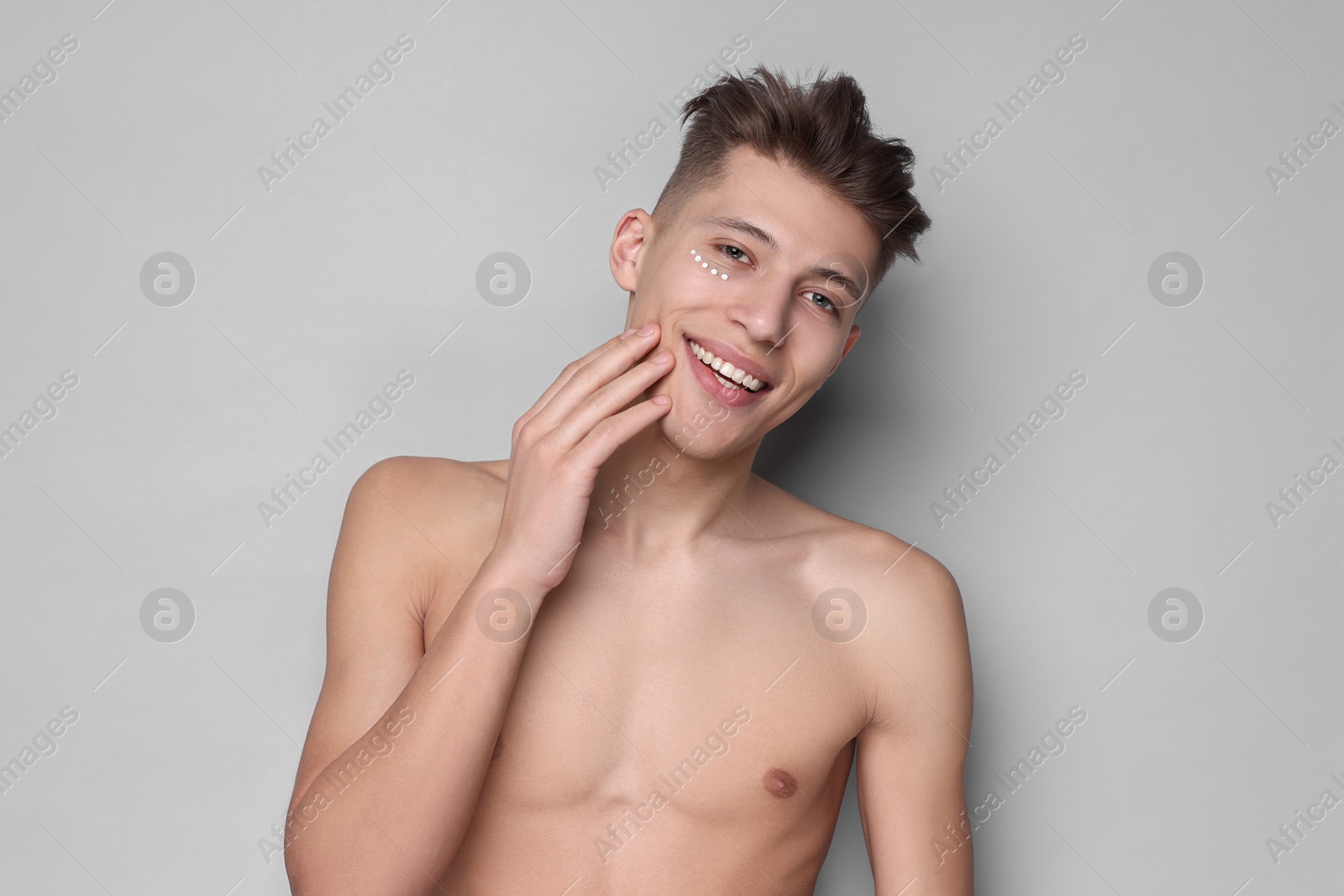 Photo of Handsome man with moisturizing cream on his face against light grey background