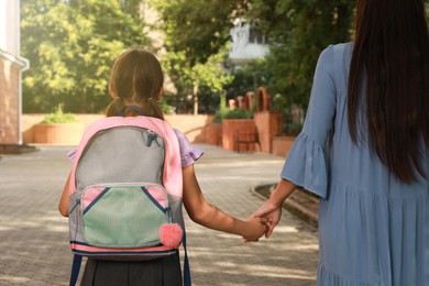 Photo of Mother taking her daughter to school, back view