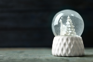 Snow globe with deer and trees on blue wooden table, space for text. Christmas season