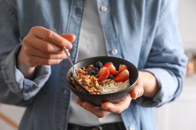 Photo of Woman eating tasty granola with berries, yogurt and seeds, closeup