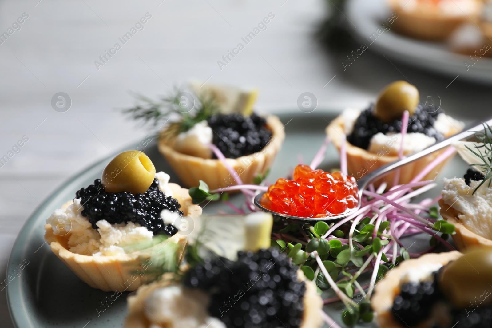 Photo of Delicious tartlets with caviar and cream cheese served on white wooden table, closeup