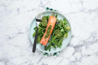 Photo of Tasty cooked salmon with pesto sauce and fresh salad served on white marble table, top view