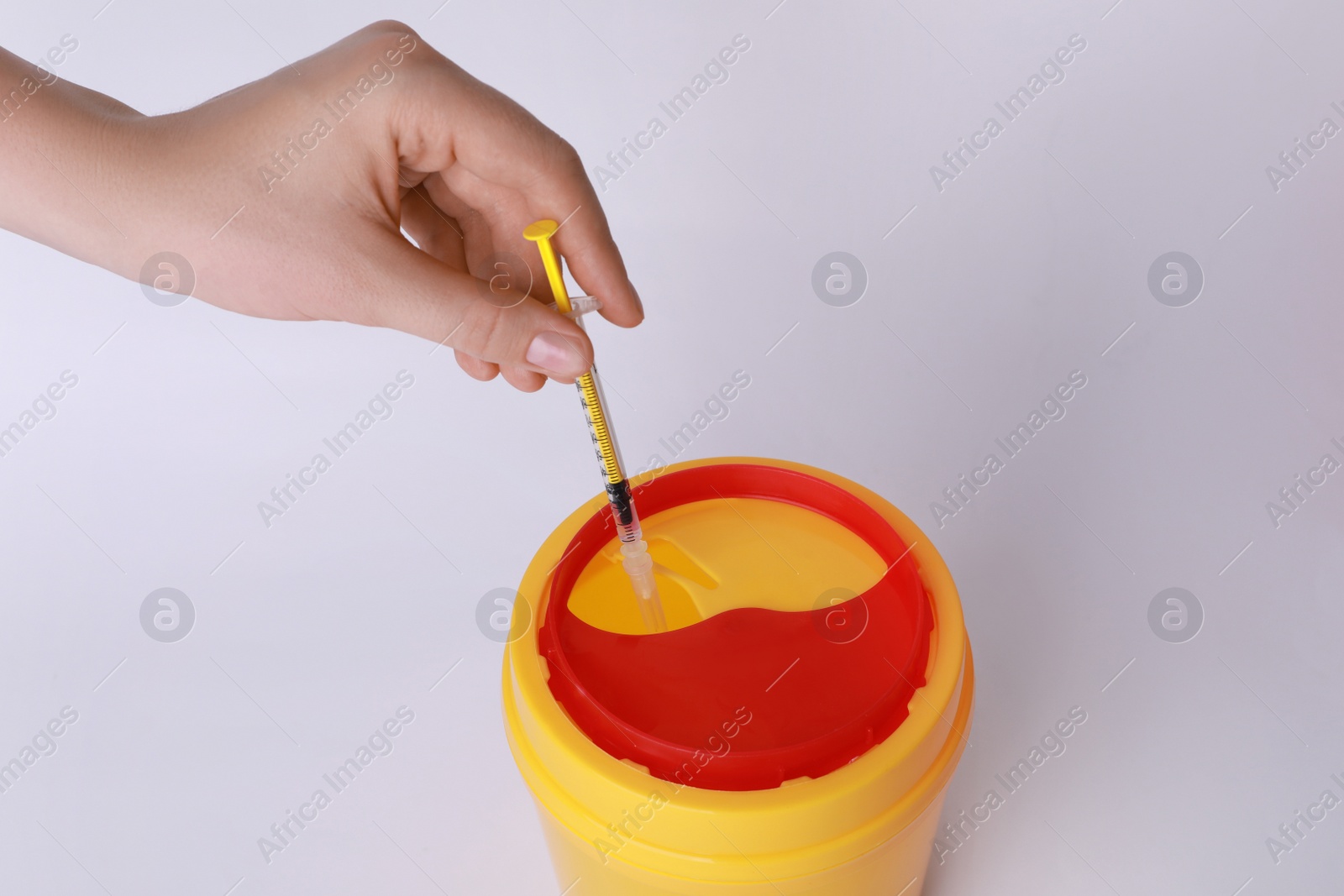 Photo of Woman throwing used syringe into sharps container on white background, closeup