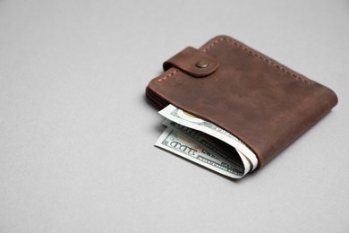 Photo of Stylish brown leather wallet with dollar banknotes on light grey background. Space for text