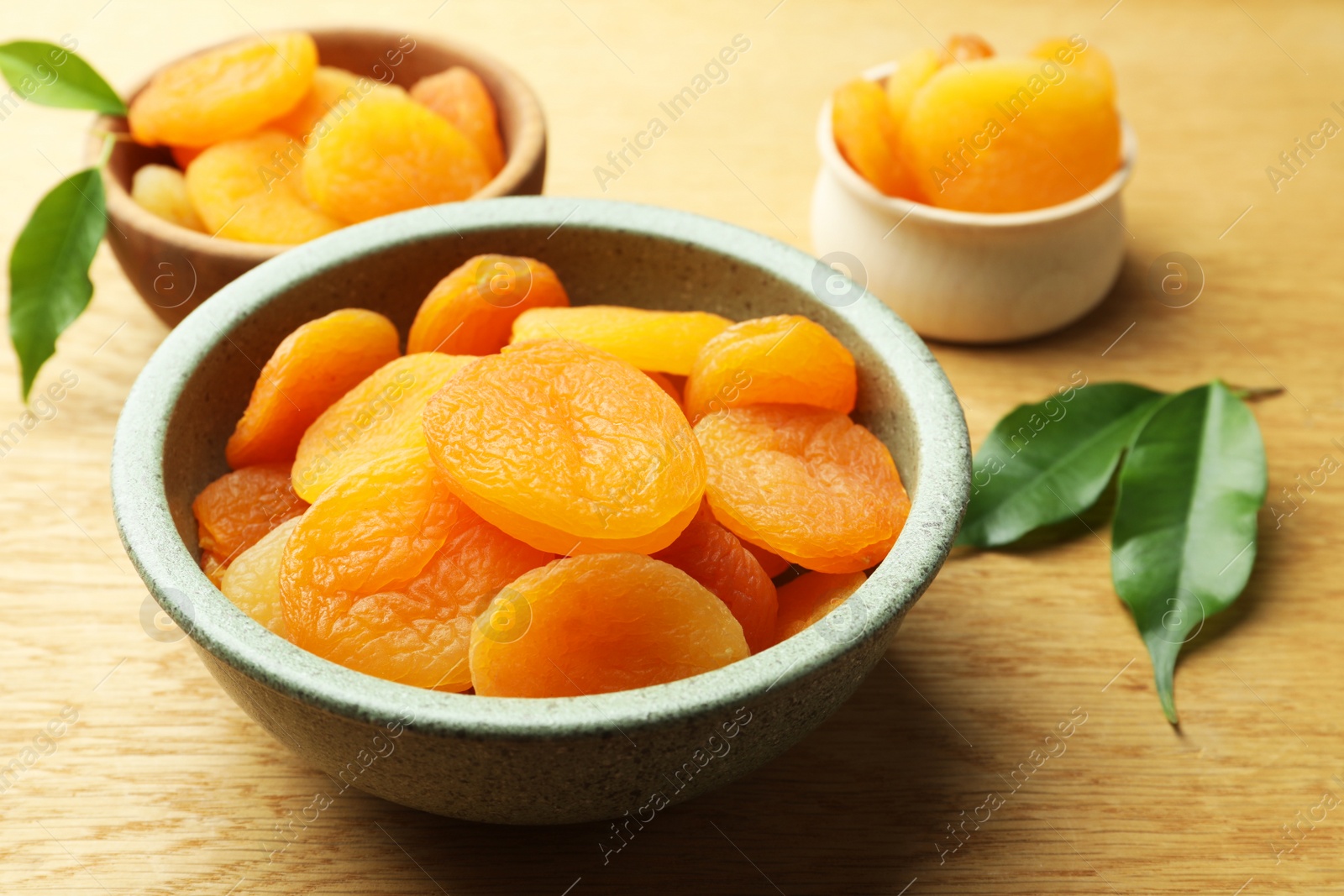 Photo of Tasty apricots with green leaves on wooden table, closeup. Dried fruits