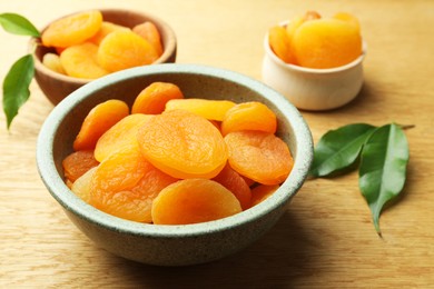 Photo of Tasty apricots with green leaves on wooden table, closeup. Dried fruits