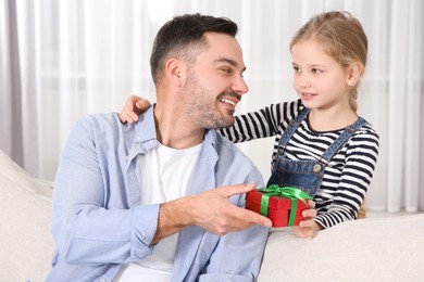 Cute little girl presenting her father with gift at home