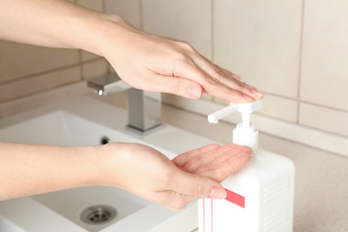 Photo of Woman applying antiseptic gel on hand in public bathroom, closeup