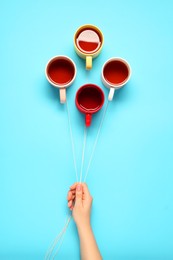 Woman holding threads with cups like balloons on light blue background, top view