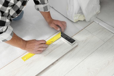 Photo of Professional worker using measuring tape during installation of laminate flooring, closeup