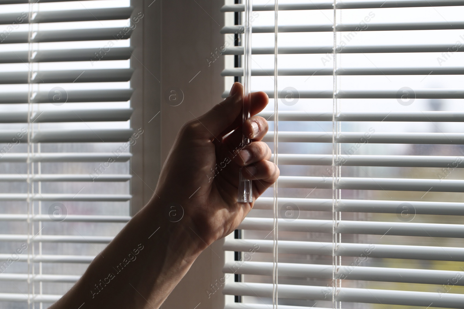 Photo of Man opening white blinds at home, closeup
