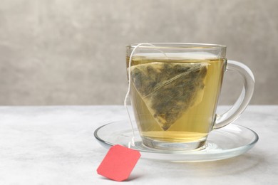Photo of Tea brewing. Glass cup with tea bag on light table, closeup. Space for text