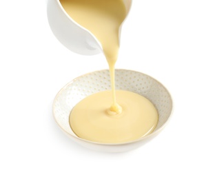 Photo of Pouring condensed milk from jug into bowl on white background. Dairy product