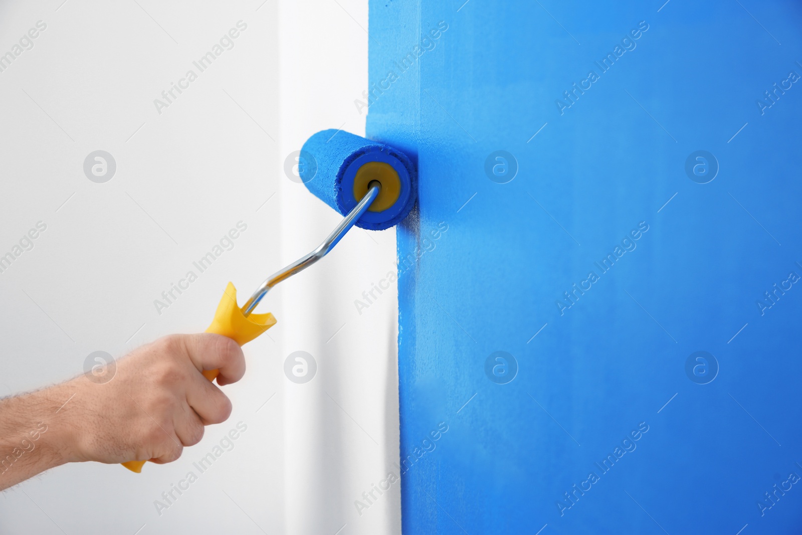 Photo of Man painting white wall with blue dye, closeup. Interior renovation