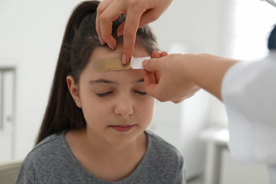 Doctor putting sticking plaster onto girl's forehead indoors