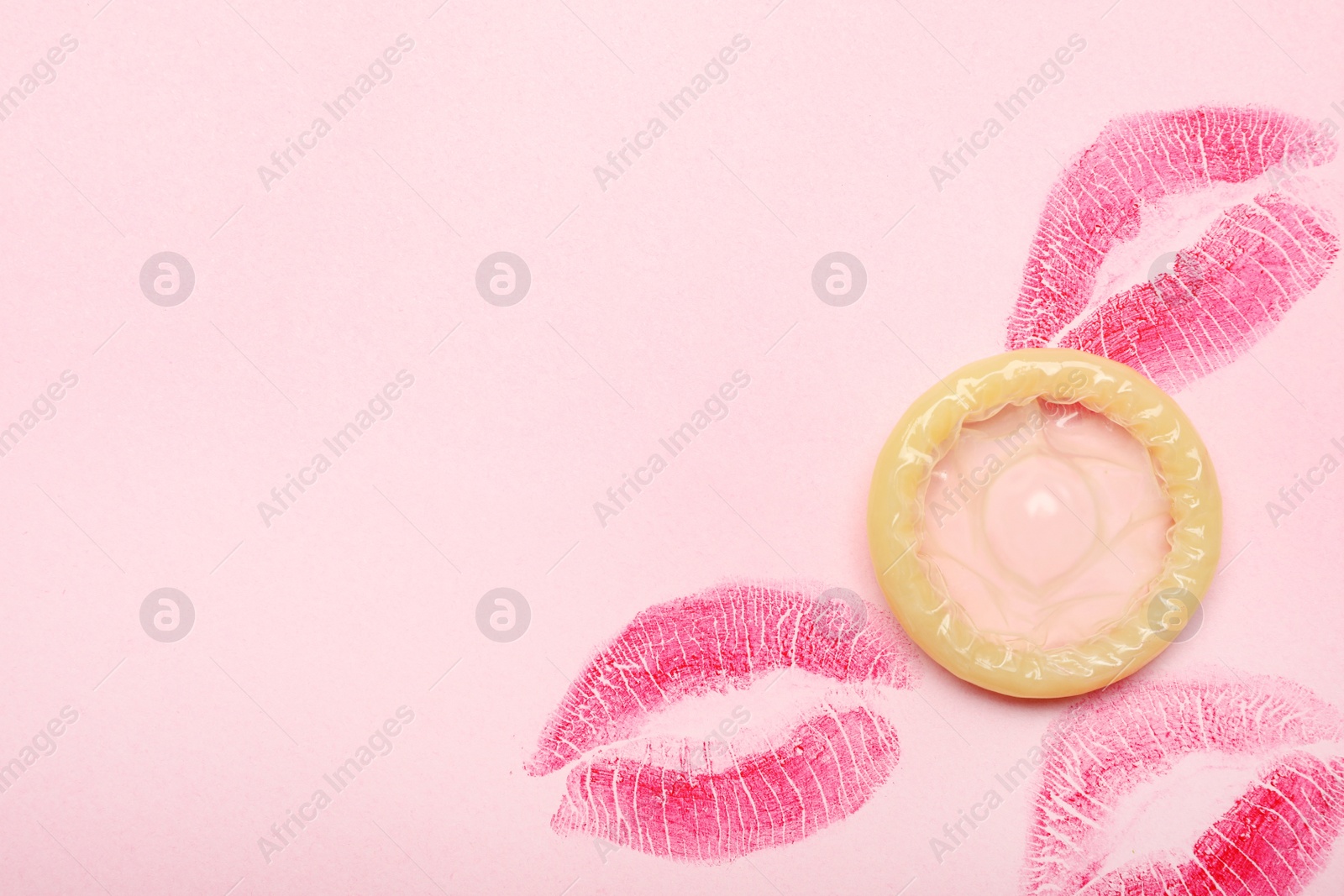 Photo of Condom with lipstick kiss marks and space for text on pink background, top view. Safe sex