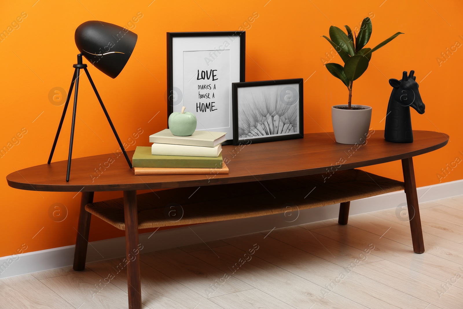 Photo of Wooden coffee table with different decor near orange wall indoors. Stylish interior design