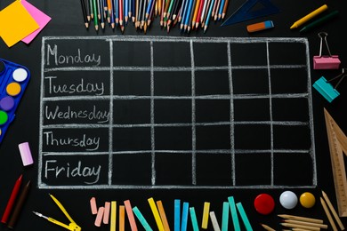 Photo of Many different stationery and drawn weekly school timetable on black chalkboard, flat lay