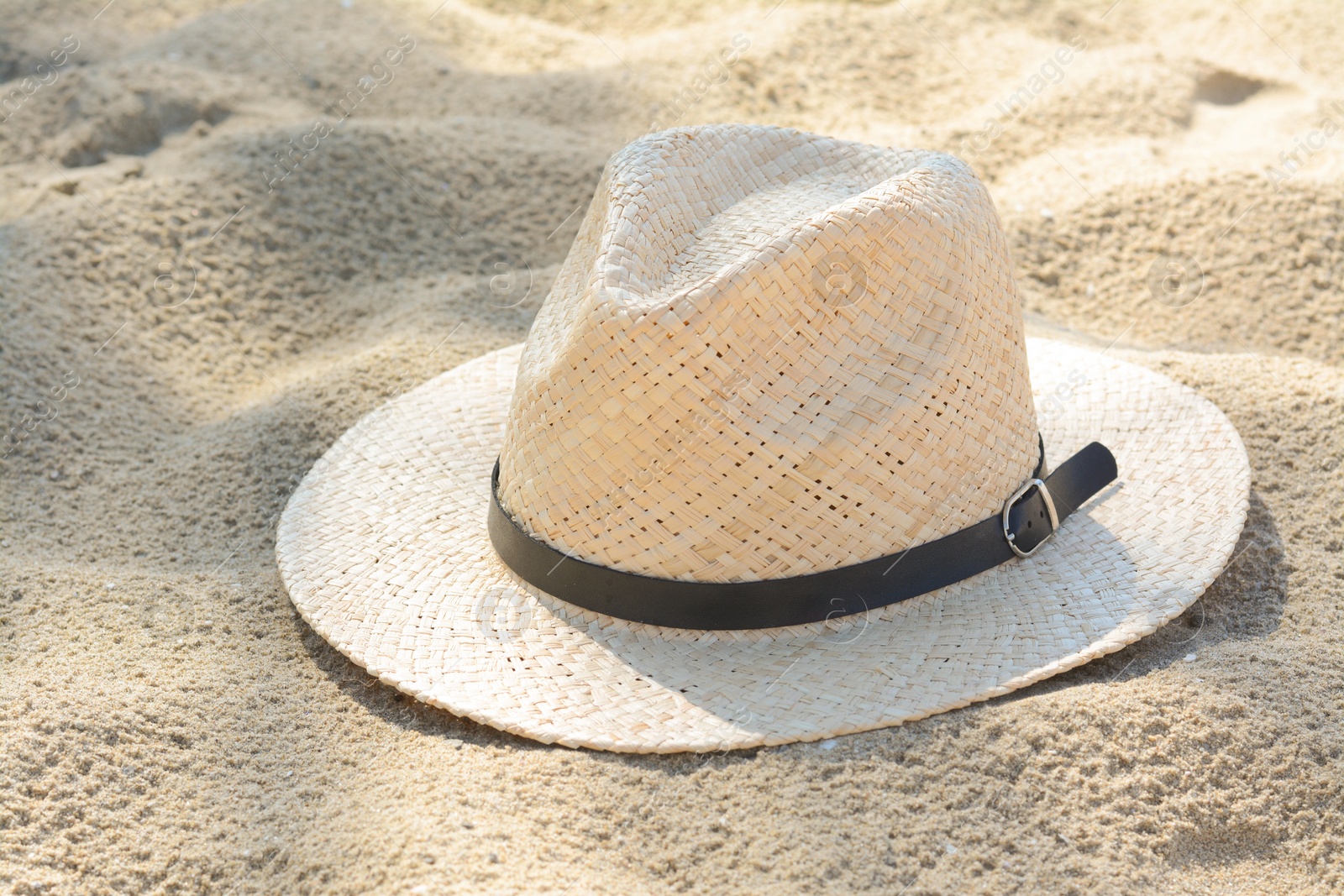 Photo of Stylish straw hat on sand outdoors. Beach accessory