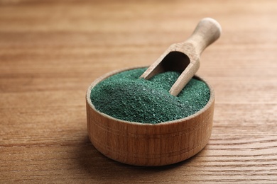 Photo of Scoop in bowl of spirulina powder on wooden table