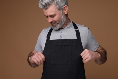 Photo of Man wearing kitchen apron on brown background. Mockup for design