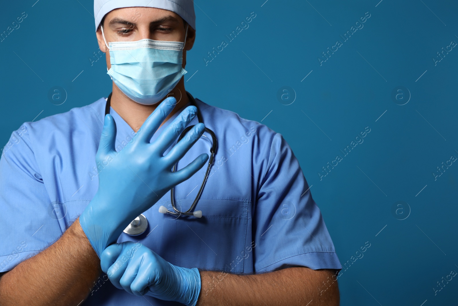 Photo of Doctor in protective mask putting on medical gloves against blue background