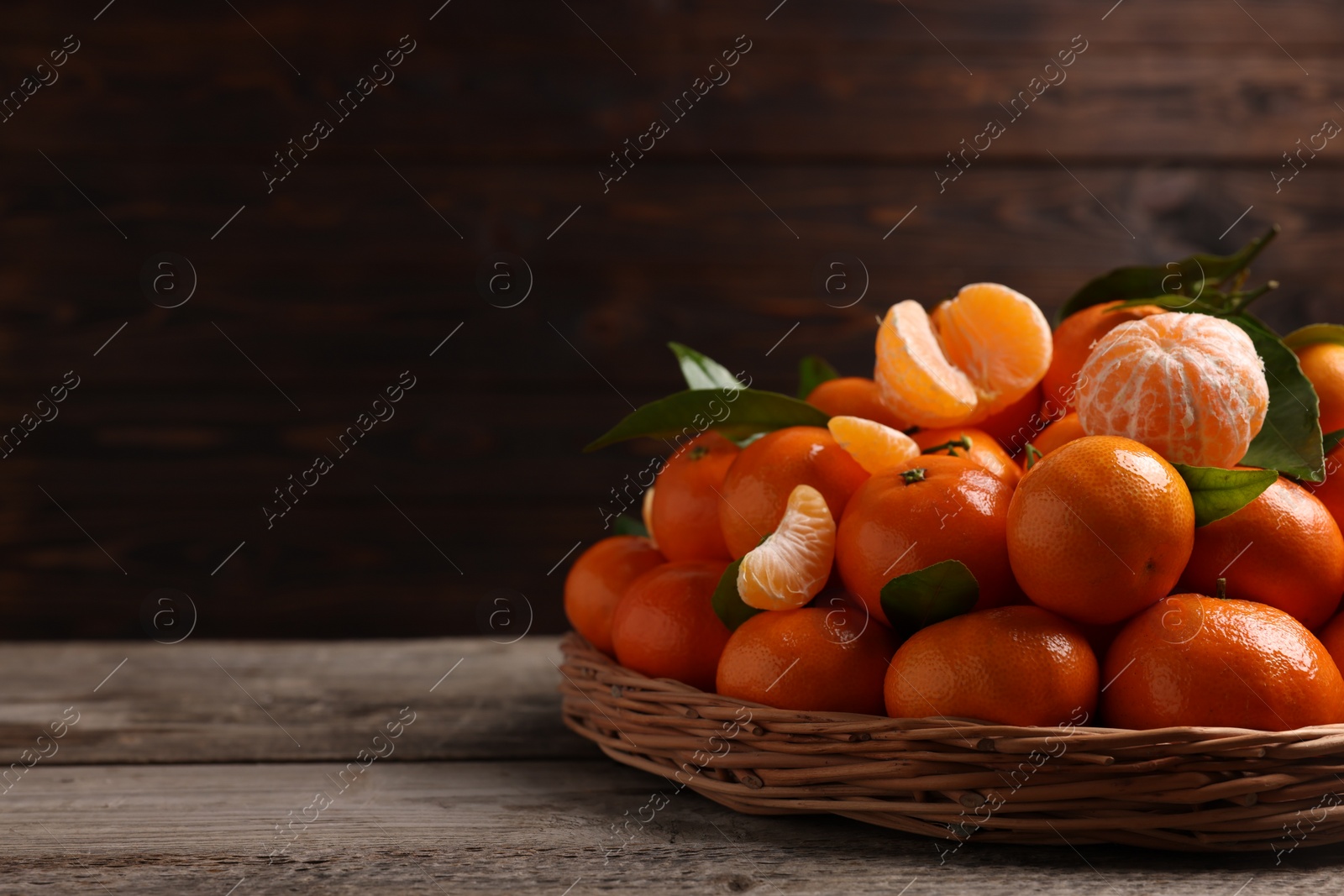 Photo of Fresh ripe juicy tangerines and green leaves on wooden table, space for text