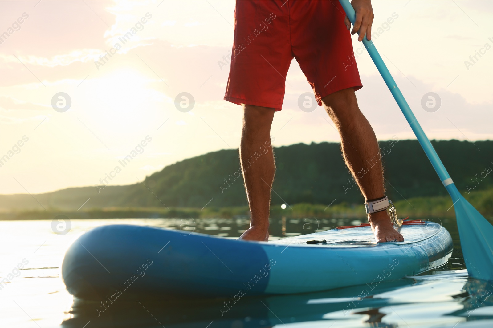 Photo of Man paddle boarding on SUP board in river at sunset, closeup