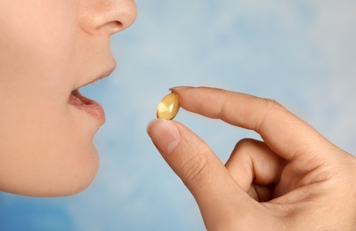 Photo of Woman taking fish oil pill on color background, closeup