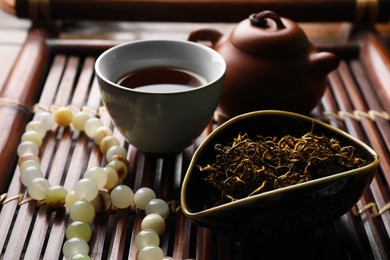 Photo of Aromatic Dianhong tea and prayer beads on wooden tray, closeup. Traditional ceremony