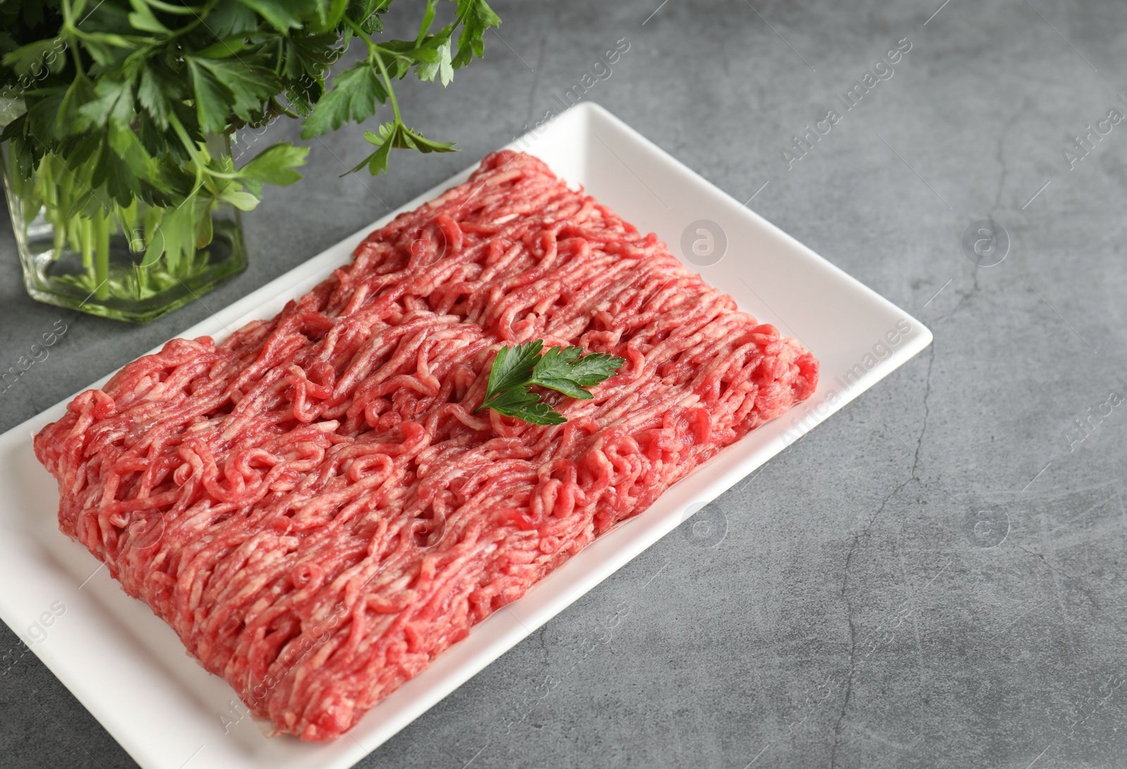 Photo of Raw ground meat and parsley on grey table