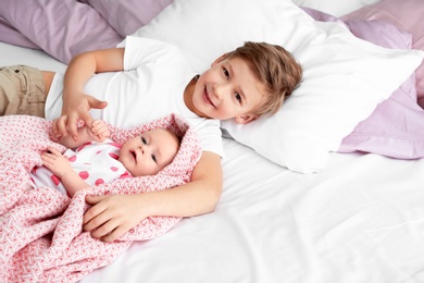 Cute little baby with elder brother lying on bed at home