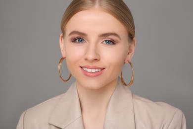 Beautiful young woman with elegant earrings on gray background