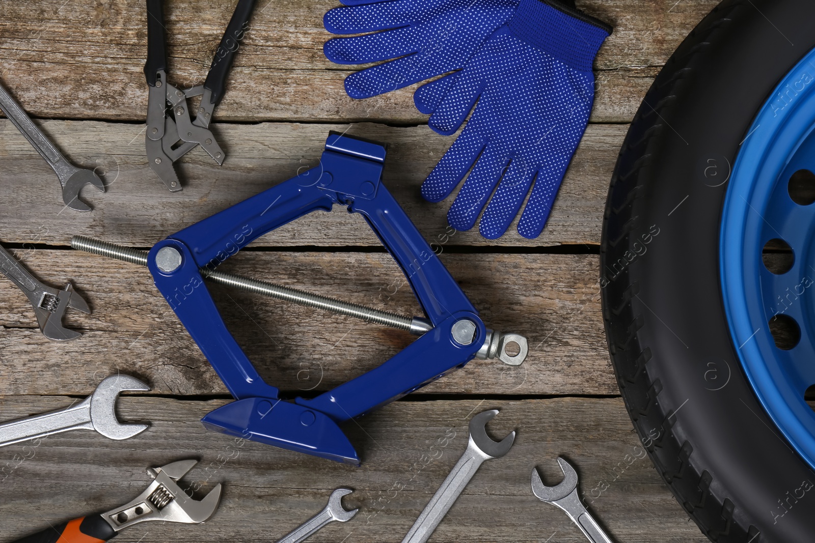 Photo of Car wheel, scissor jack, gloves and different tools on wooden surface, flat lay