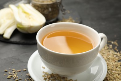 Photo of Aromatic fennel tea in cup and seeds on black table, closeup