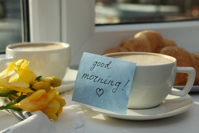Photo of Coffee, flowers and card with phrase GOOD MORNING! near window