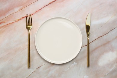 Photo of Clean plate and golden cutlery on beige marble table, flat lay